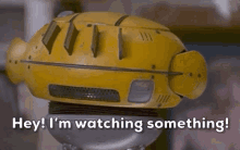 a close up of a yellow robot with the words `` hey ! i 'm watching something '' written on it .