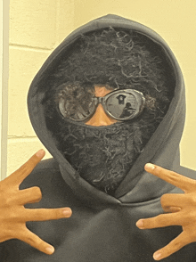 a person wearing a black hoodie and goggles is making a peace sign with their hands