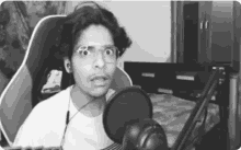 a black and white photo of a man wearing glasses and headphones in front of a microphone .