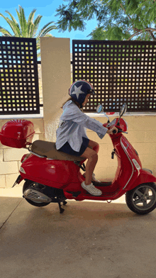 a woman wearing a helmet sits on a red vespa