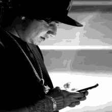 a black and white photo of a man wearing a hat looking at his phone