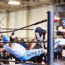 a wrestler wearing a mask that says ' skull ' on it is hanging upside down in a wrestling ring