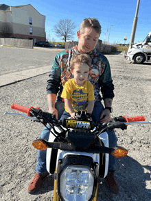 a man is holding a little boy on a motorcycle with a protaper handlebars