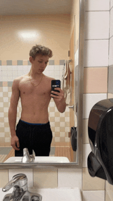 a shirtless man taking a selfie in a bathroom mirror