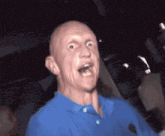 a bald man in a blue shirt is making a funny face in a dark room .