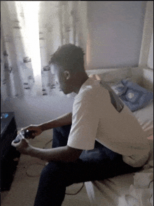 a man sitting on a bed playing a video game with a controller