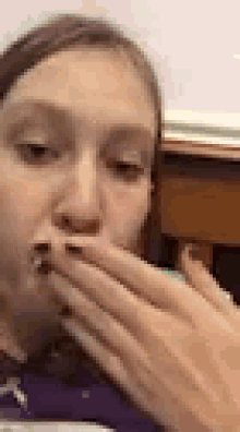 a close up of a woman covering her mouth with her hand while eating .