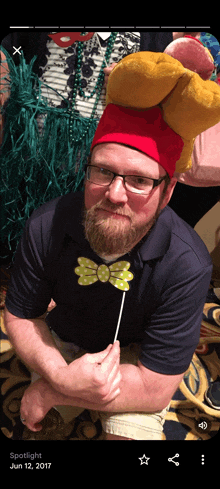 a man with a beard wearing a red hat and glasses is holding a bow tie