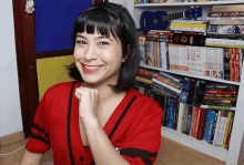 a woman in a red shirt is smiling in front of a bookshelf full of books including one that says ' asimov '