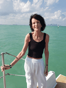 a woman in a black top and white pants stands on a boat in the ocean