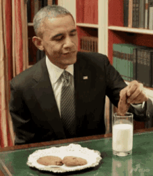 a man in a suit and tie is sitting at a desk with a plate of cookies and a glass of milk