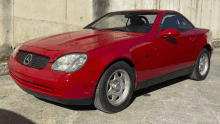 a red mercedes convertible is parked in front of a wall