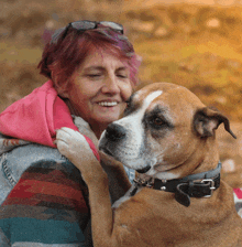 a woman in a pink hoodie is hugging a brown and white dog