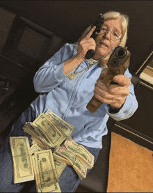 a woman is holding a gun and talking on a cell phone while laying on a pile of 20 dollar bills