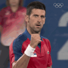 a man in a red and blue shirt is holding his fist in the air while wearing a wristband .