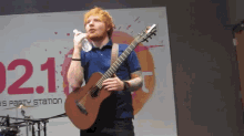 a man singing into a microphone while holding a guitar in front of a sign that says ' 021 '