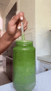 a person is pouring green liquid into a mason jar with a straw