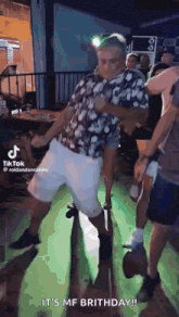 a man in a floral shirt is dancing in a crowd of people .