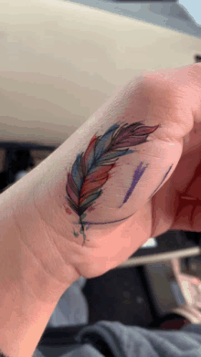 a close up of a person 's wrist with a colorful feather tattoo