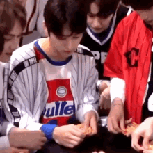 a group of young men are sitting around a table eating pizza . one of the men is wearing a baseball jersey .