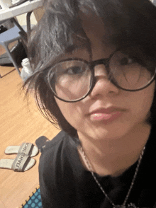 a woman wearing glasses and a necklace has a pair of slippers on the floor
