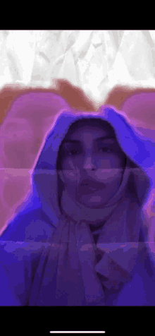 a woman wearing a hijab and a hooded sweatshirt is standing in front of a purple background .