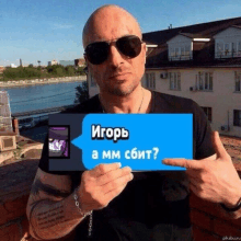 a bald man wearing sunglasses holds up a sign that says " igor " on it