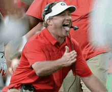 a man wearing a red shirt and a white hat with the letter g on it is giving a thumbs up