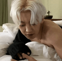 a shirtless man with white hair is laying on a bed with his hand on a pillow