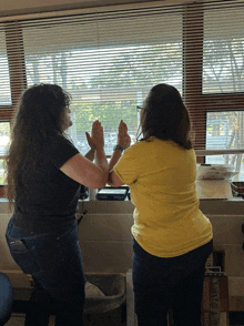 two women giving each other a high five in front of a window with blinds