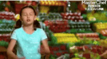 a little girl is standing in front of a display of fruits and vegetables with the words masterchef junior tuesdays at the bottom