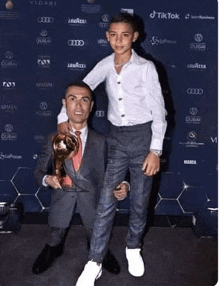 a man in a suit holds a trophy next to a boy