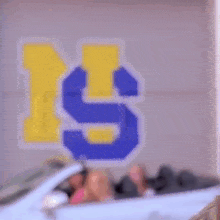 three women are sitting in a white convertible car in front of a wall with the letter s painted on it .