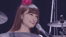 a woman is playing drums and singing into a microphone while wearing a pink flower in her hair .