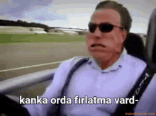 a man wearing sunglasses is driving a car with the words kanka orda firlatma vard written below him