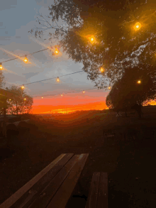 a picnic table in front of a sunset with string lights