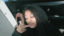 a woman wearing a black hoodie is making a peace sign with her finger