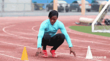 a woman in a blue jacket is squatting on a track in front of a yellow cone that says sugar on it