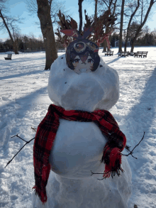 a snowman wearing a scarf and goggles has a picture of a girl on his head