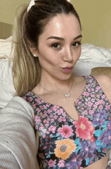 a woman wearing a floral top and a butterfly necklace takes a selfie