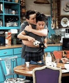 a man and woman are hugging each other in a kitchen while sitting at a table .