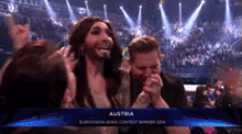 a man with a beard and a woman with long hair are sitting in a stadium with a sign that says austria