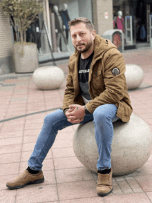 a man wearing a black shirt with the word luxlo on it sits on a bench