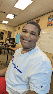 a boy wearing a white champion t-shirt smiles in front of a white board that says explorer