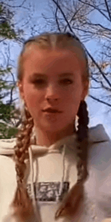 a young girl with braids in her hair is wearing a white hoodie .