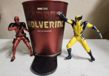 deadpool and wolverine action figures standing next to a bucket that says deadpool wolverine only in theatres