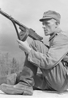 a black and white photo of a soldier sitting down holding a gun .