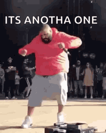 a man in a red hoodie is dancing in front of a crowd with the words `` its anotha one '' .