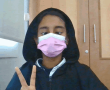 a girl wearing a pink face mask and a black hoodie is giving a peace sign