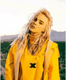 billie eilish is wearing a yellow jacket with a black x on it .